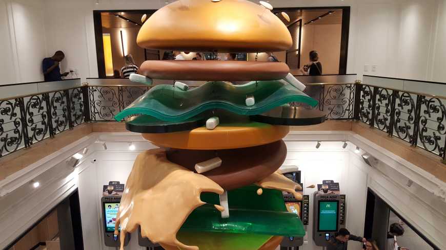 Enorme Big Mac pendurado no salão e abaixo, máquinas de autoatendimento
